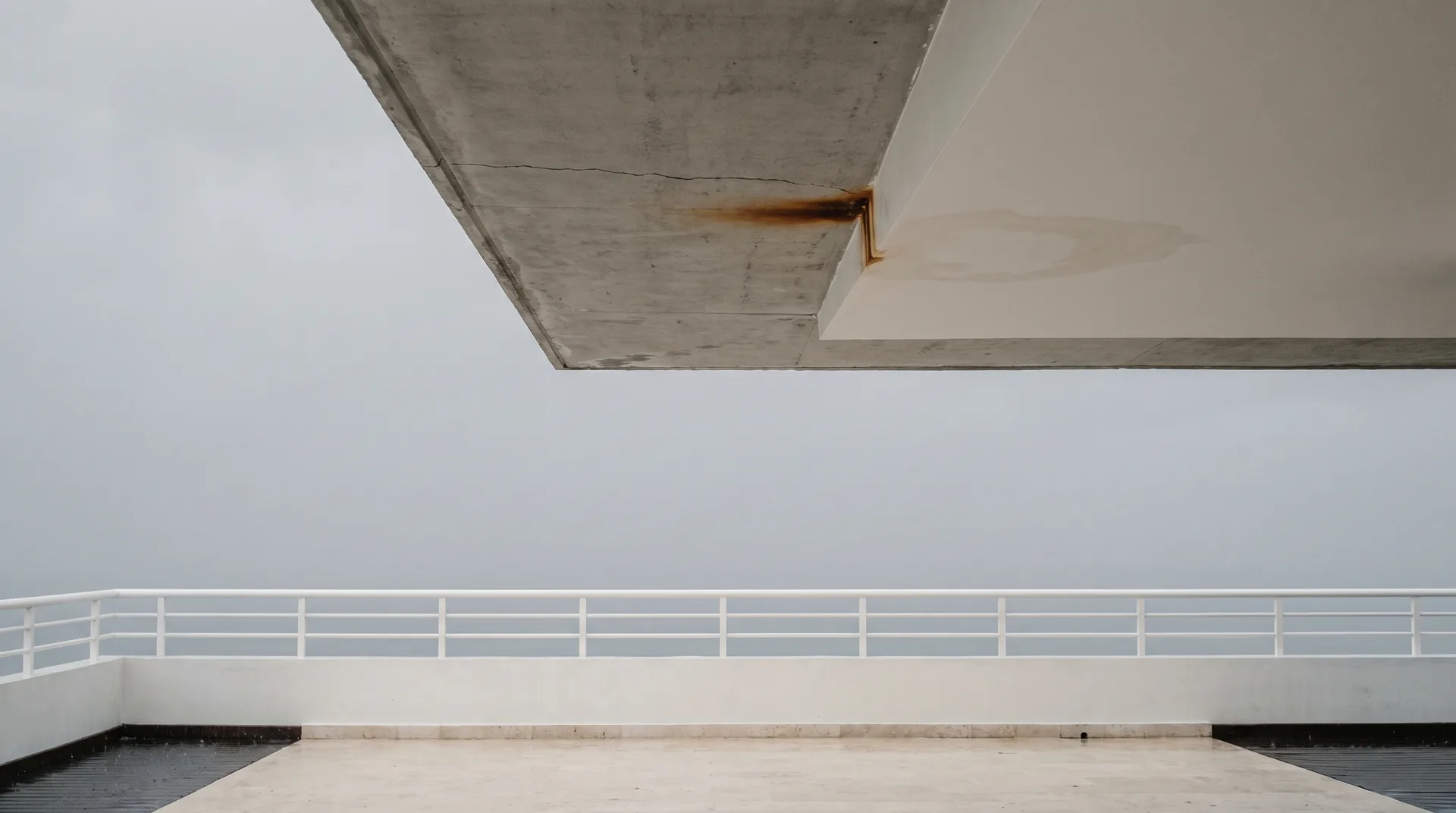 El techo de concreto aparente de una terraza cubierta en Cancún, con una mancha de óxido que asoma en una fisura junto al borde y el aire gris de la temporada de lluvias.