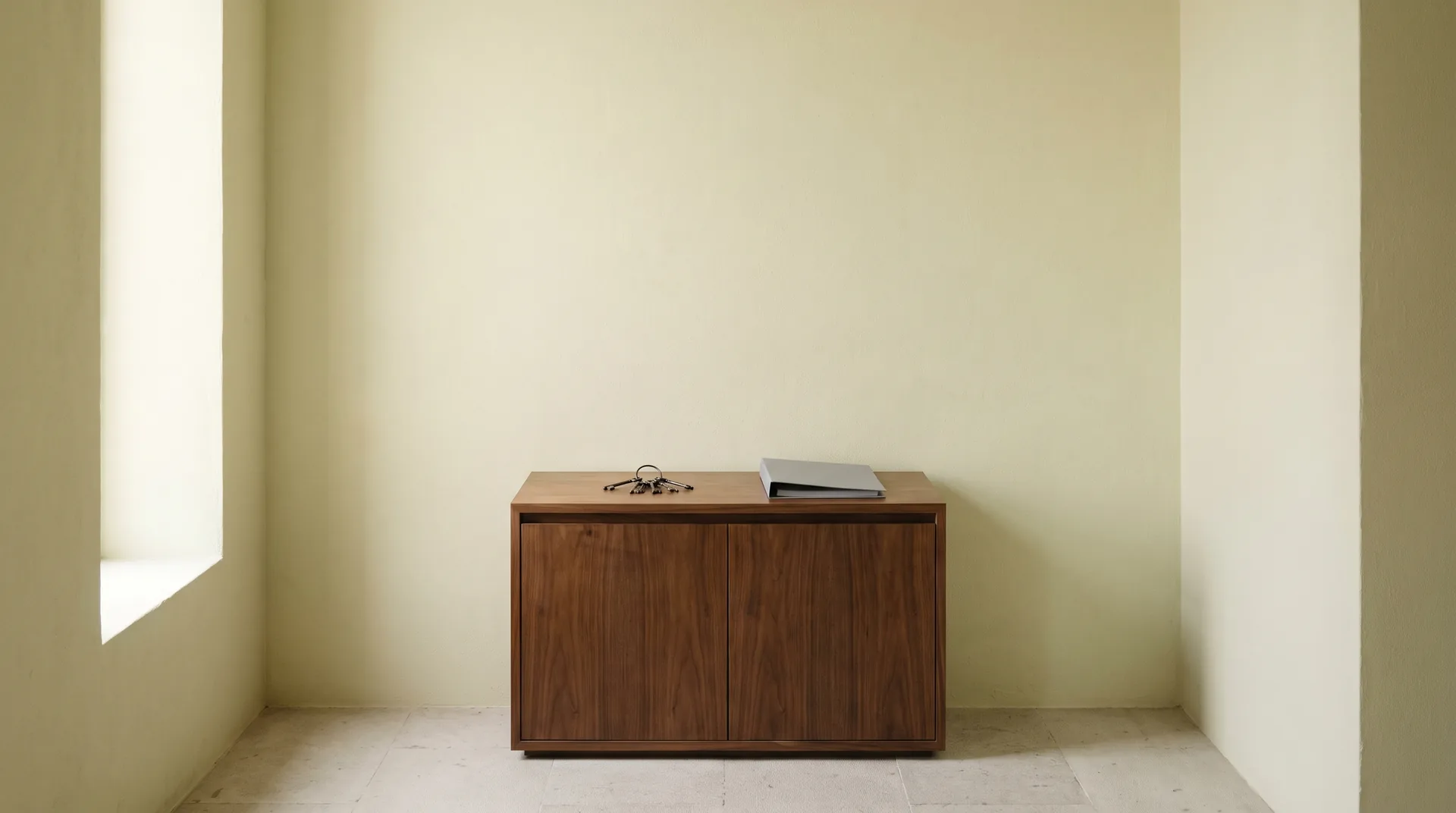 A closed hallway cabinet in a quiet Mexican house, with a single ring of keys and a plain folder resting on its top in soft daylight.