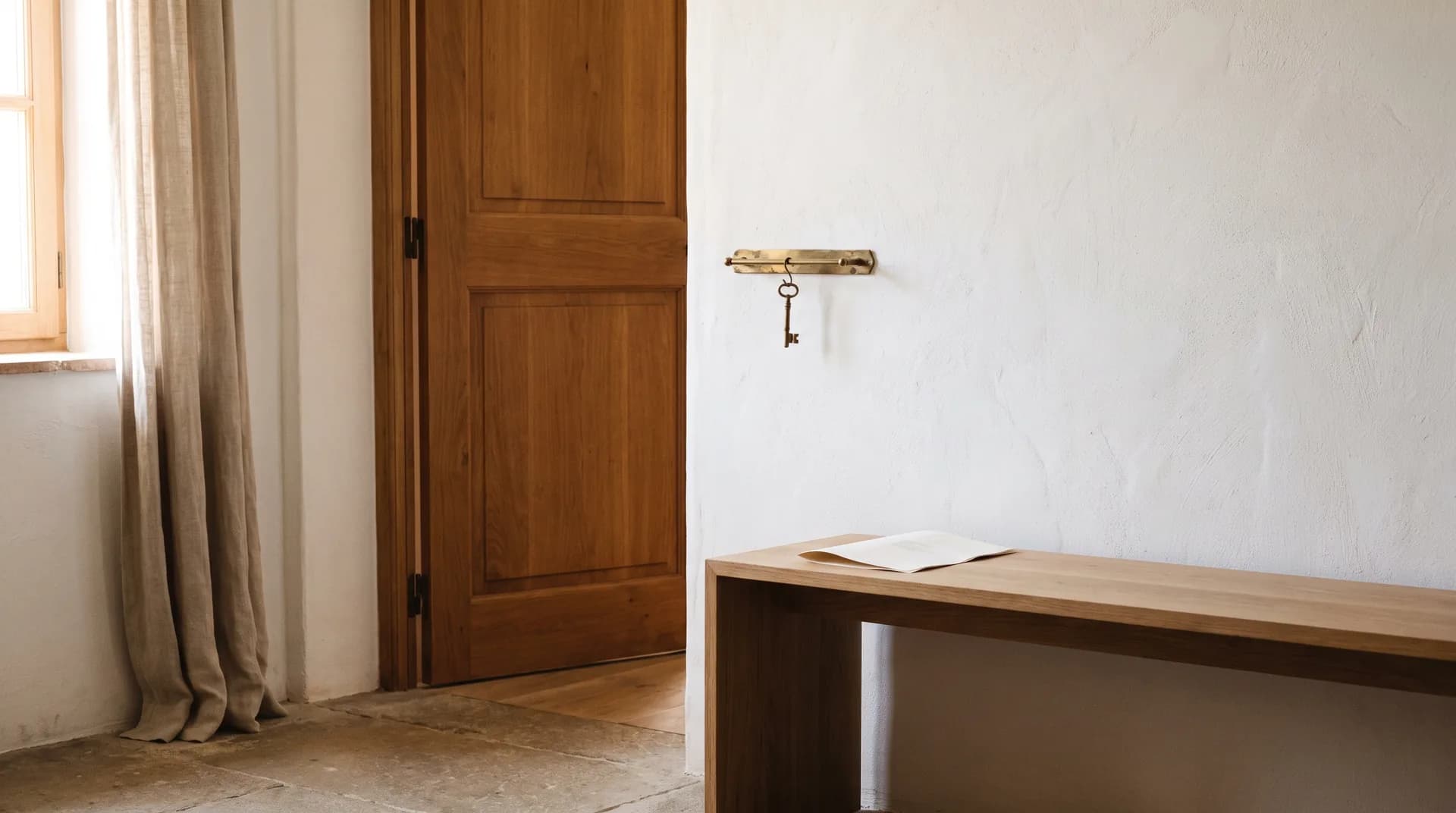 Entrada de una casa particular vista desde dentro, con la puerta de madera entornada y una sola llave colgada de un gancho de latón.