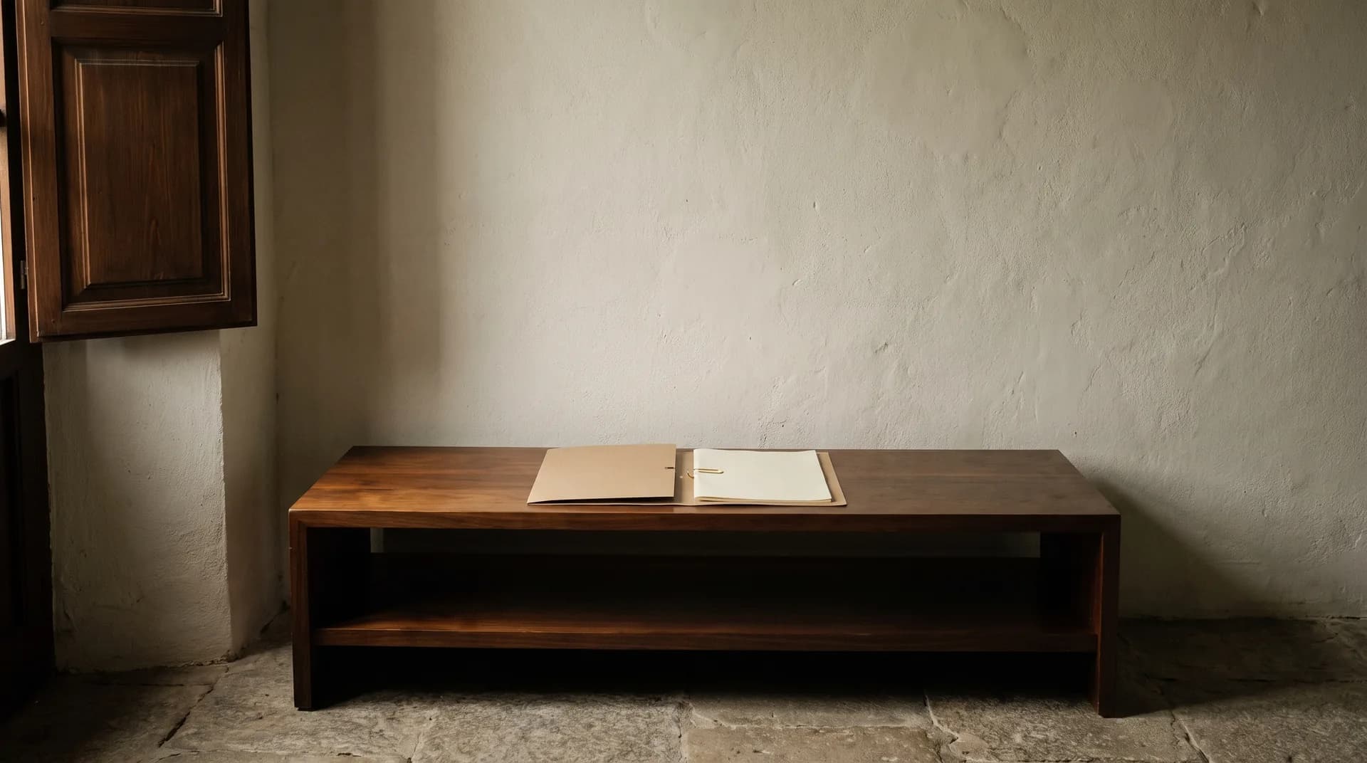 Una consola de madera junto a una ventana entornada, con una carpeta cerrada de cartón y un clip de latón encima.