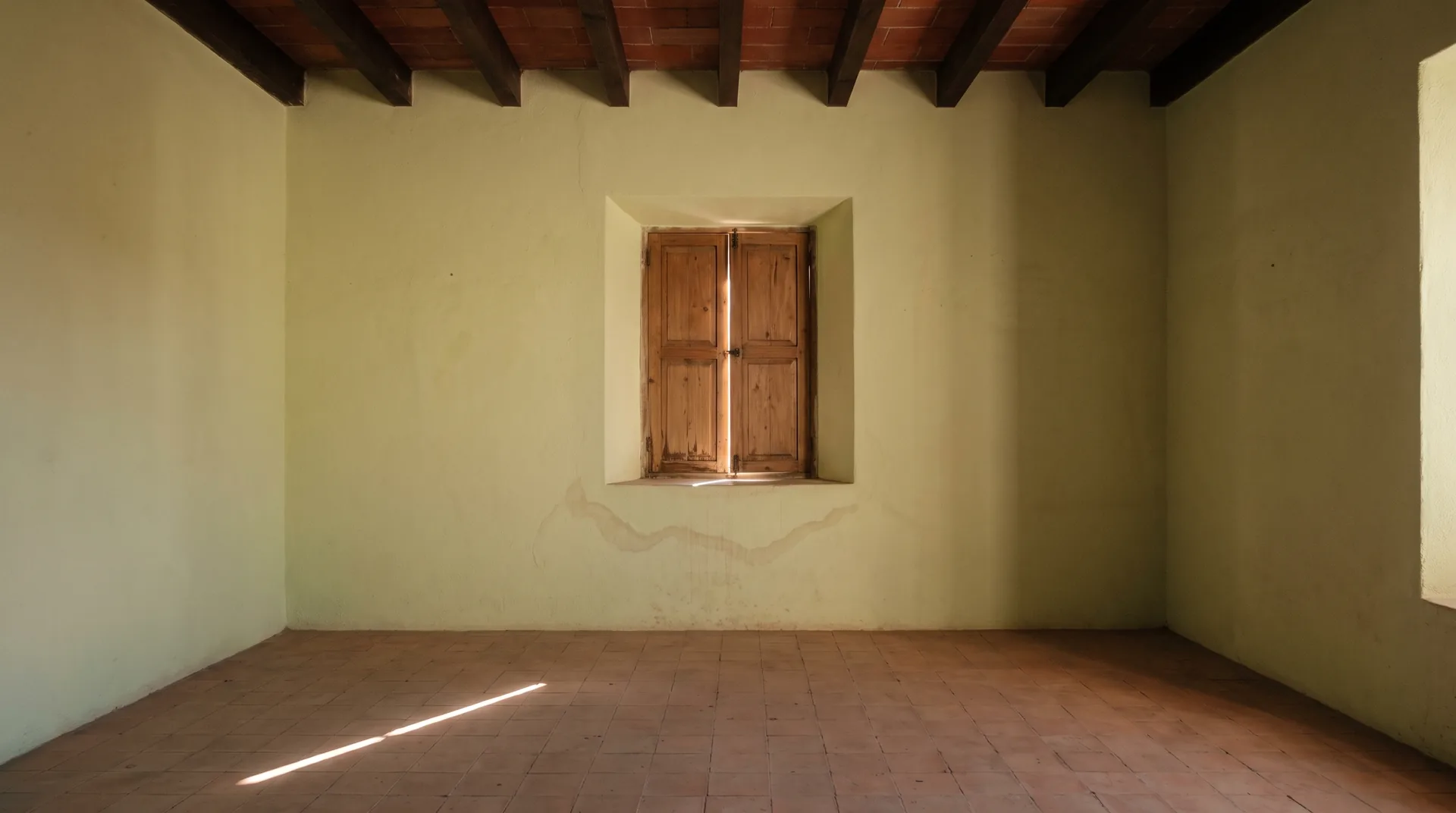 An empty room in an old stone house in San Miguel de Allende on a winter morning, with a blade of low sun between closed shutters and a faint dried damp stain on the lime plaster.